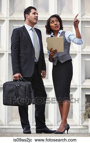 Stock Image - Full length view of business people standing talking, pointing upwards, looking up. Fotosearch