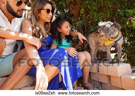 Stock Image - Girl and parents sitting in garden with dog. Fotosearch