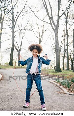 Stock Image - Girl playing with skipping rope, looking at camera, arms raised. Fotosearch