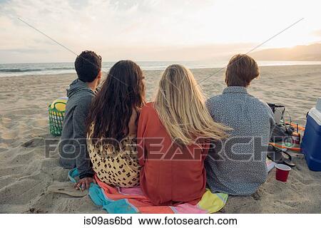 Stock Image - Group of friends having picnic on beach, rear view. Fotosearch