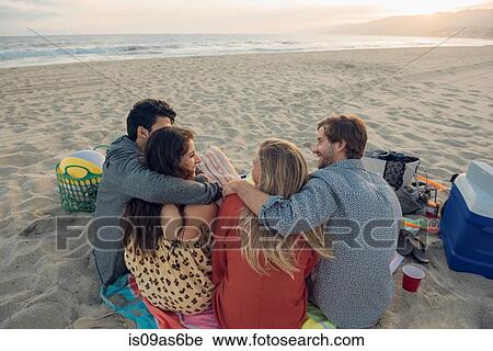 Stock Image - Group of friends having picnic on beach, rear view. Fotosearch