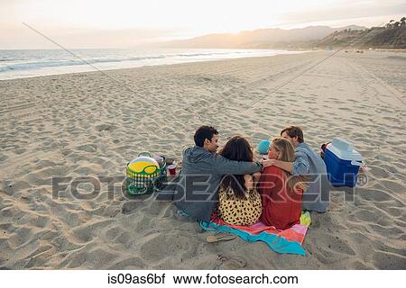 Stock Image - Group of friends having picnic on beach, rear view. Fotosearch