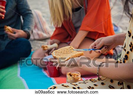 Stock Image - Group of friends having picnic on beach, mid section. Fotosearch