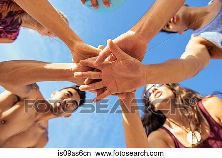 Picture - Group of friends joining hands on beach, low angle view. Fotosearch