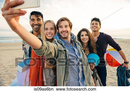 Picture - Group of friends on beach, taking self portrait with smartphone. Fotosearch