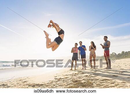 Group of friends on beach watching friend leap in air View Large Photo Image Stock Image - Group of friends on beach watching friend leap in air. Fotosearch