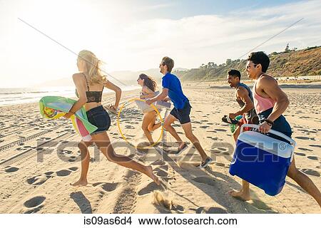 Picture - Group of friends running on beach, rear view. Fotosearch