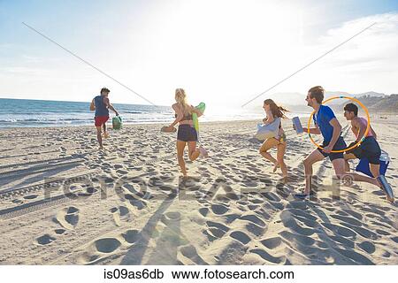 Stock Image - Group of friends running on beach, rear view. Fotosearch