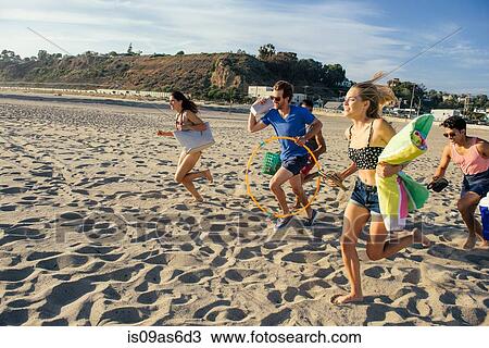 Stock Image - Group of friends running on beach. Fotosearch