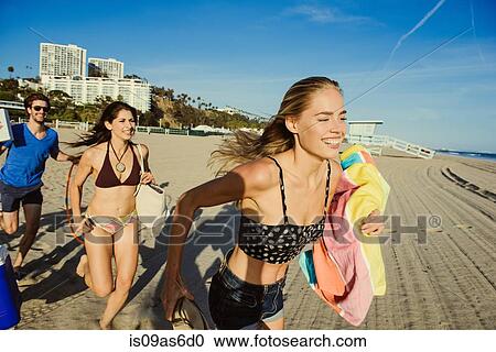 Stock Image - Group of friends, running towards beach. Fotosearch