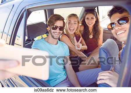 Stock Photo - Group of friends sitting in car, taking self portrait with smartphone, laughing. Fotosearch