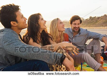 Stock Image - Group of friends sitting together on beach. Fotosearch