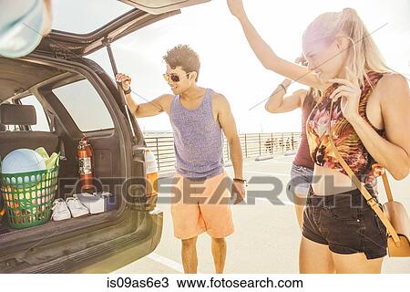 Stock Image - Group of friends standing by car, at beach. Fotosearch