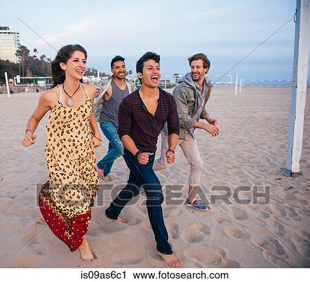 Stock Image - Group of friends walking along beach, laughing. Fotosearch