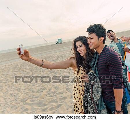 Group of friends walking along beach, young couple taking self portrait with smartphone View Large Photo Image Stock Photo - Group of friends walking along beach, young couple taking self portrait with smartphone. Fotosearch