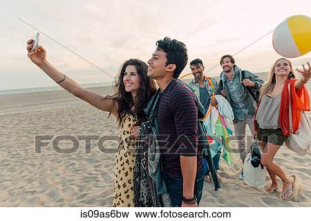 Group of friends walking along beach, young couple taking self portrait with smartphone View Large Photo Image Stock Photo - Group of friends walking along beach, young couple taking self portrait with smartphone. Fotosearch