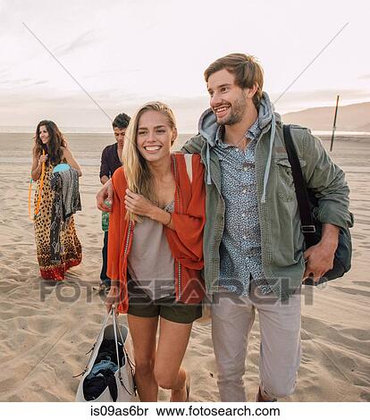 Group of friends walking along beach, young couple looking at smartphone View Large Photo Image Stock Photography - Group of friends walking along beach, young couple looking at smartphone. Fotosearch
