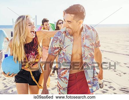 Stock Image - Group of friends walking on beach, ready for picnic. Fotosearch