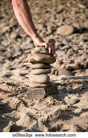 Hand of young man placing stone on stone stack at beach View Large Photo Image Stock Image - Hand of young man placing stone on stone stack at beach. Fotosearch