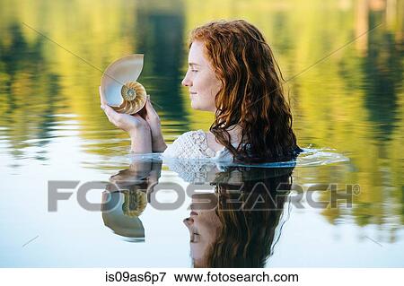 Head and shoulders of young woman with long red hair in lake gazing at seashell View Large Photo Image Stock Photo - Head and shoulders of young woman with long red hair in lake gazing at seashell. Fotosearch