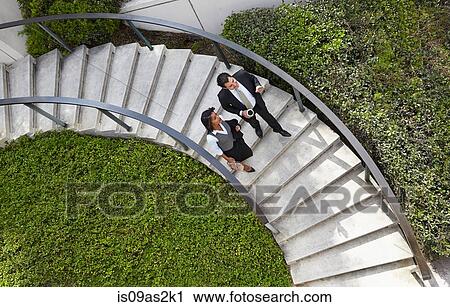 Stock Image - High angle view of business people descending spiral stairway. Fotosearch