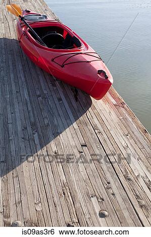 Stock Photograph - High angle view of kayak and paddle on wooden pier next to water. Fotosearch