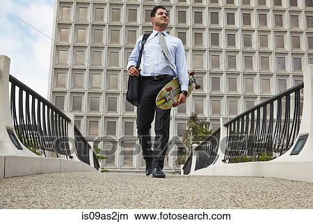 Low angle full length front view of mid adult business man carrying skateboard View Large Photo Image Picture - Low angle full length front view of mid adult business man carrying skateboard. Fotosearch