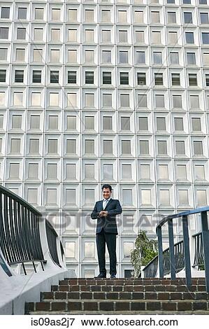 Low angle view of business man standing at top of stairway looking at watch View Large Photo Image Stock Photo - Low angle view of business man standing at top of stairway looking at watch. Fotosearch
