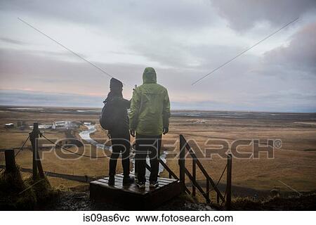 Stock Image - Male and female tourists taking photographs from viewing platform at Seljalandsfoss, Iceland. Fotosearch