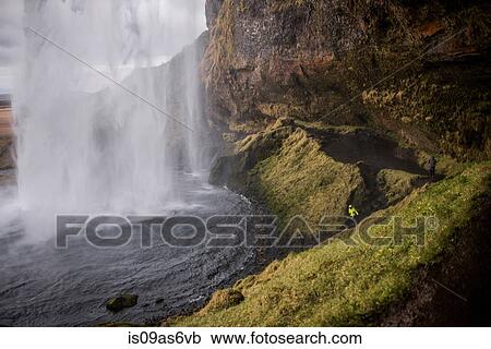 Stock Image - Male tourist at Seljalandsfoss waterfall, Iceland. Fotosearch