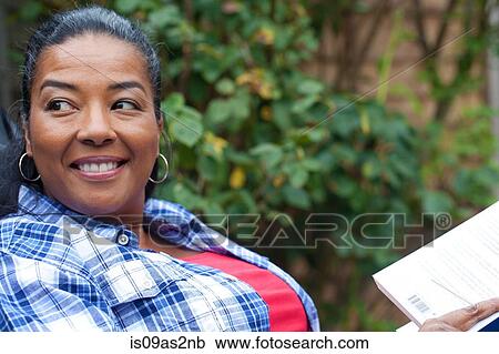 Stock Image - Mature woman looking sideways from reading book in garden. Fotosearch