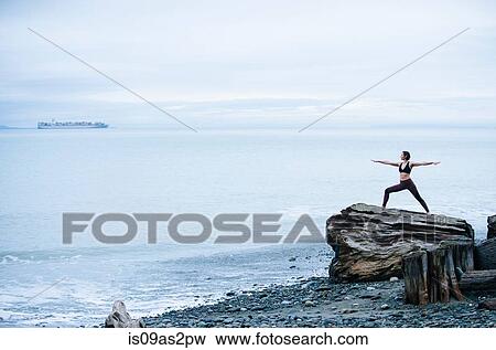 Mature woman practicing yoga pose whilst standing on large driftwood tree stump on beach View Large Photo Image Stock Photo - Mature woman practicing yoga pose whilst standing on large driftwood tree stump on beach. Fotosearch