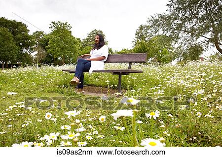 Mature woman sitting on bench in daisy filled park View Large Photo Image Picture - Mature woman sitting on bench in daisy filled park. Fotosearch