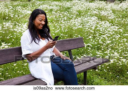 Picture - Mature woman sitting on park bench reading smartphone text. Fotosearch
