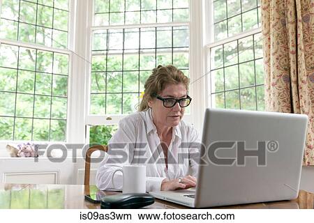 Mature woman working on laptop in living room View Large Photo Image Picture - Mature woman working on laptop in living room. Fotosearch
