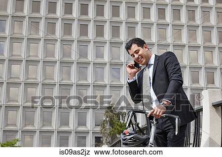 Mid adult business man holding bicycle, making telephone call using smartphone View Large Photo Image Stock Photo - Mid adult business man holding bicycle, making telephone call using smartphone. Fotosearch