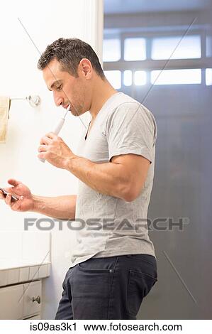 Mid adult man, brushing teeth, looking at mobile phone View Large Photo Image Stock Image - Mid adult man, brushing teeth, looking at mobile phone. Fotosearch
