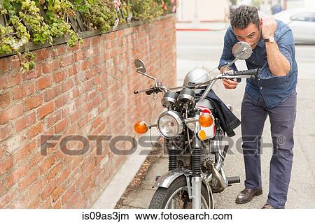 Picture - Mid adult man checking hair in motorbike side mirror. Fotosearch