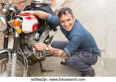 Mid adult man crouching beside motorbike View Large Photo Image Picture - Mid adult man crouching beside motorbike. Fotosearch