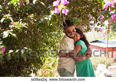 Stock Image - Mid adult man hugging daughter in garden. Fotosearch