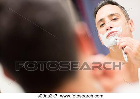 Stock Photo - Mid adult man, looking in mirror, shaving. Fotosearch
