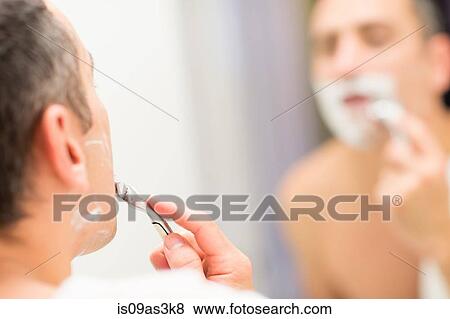 Stock Photo - Mid adult man, looking in mirror, shaving. Fotosearch