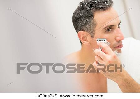 Stock Photo - Mid adult man, looking in mirror, shaving. Fotosearch