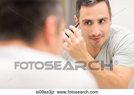 Stock Photo - Mid adult man, looking in mirror, using tweezers. Fotosearch