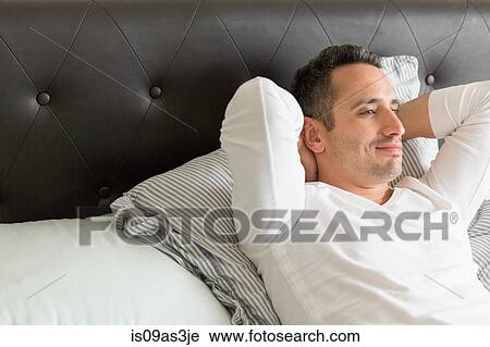 Stock Image - Mid adult man relaxing on bed. Fotosearch