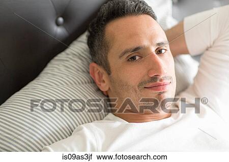 Stock Image - Mid adult man relaxing on bed. Fotosearch