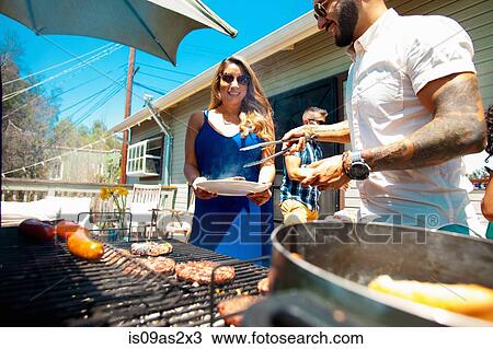 Stock Image - Mid adult man serving barbecue food to family in garden. Fotosearch