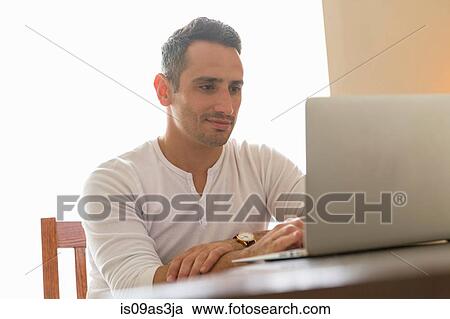 Mid adult man sitting at desk, using laptop View Large Photo Image Stock Image - Mid adult man sitting at desk, using laptop. Fotosearch