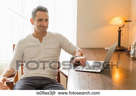 Stock Photo - Mid adult man sitting at desk, using laptop. Fotosearch