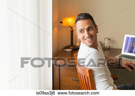 Mid adult man sitting at desk, using laptop View Large Photo Image Stock Photograph - Mid adult man sitting at desk, using laptop. Fotosearch